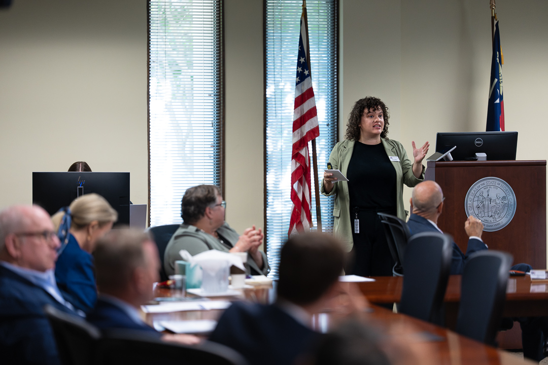 Woman at the front of a board room speaking.