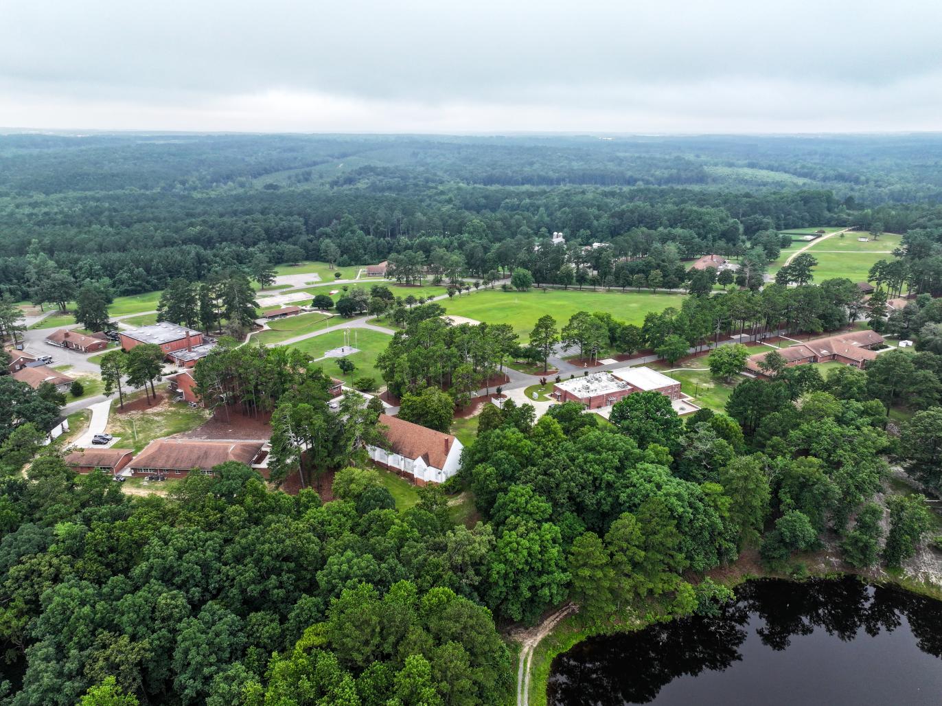 Aerial view of a campus with several buildings, trees and a lake.