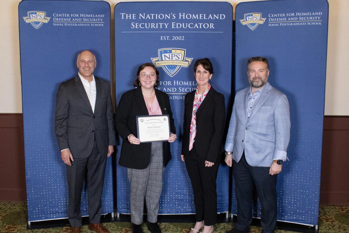 Four people stand in front of a blue backdrop. One female in the center holds a certificate.