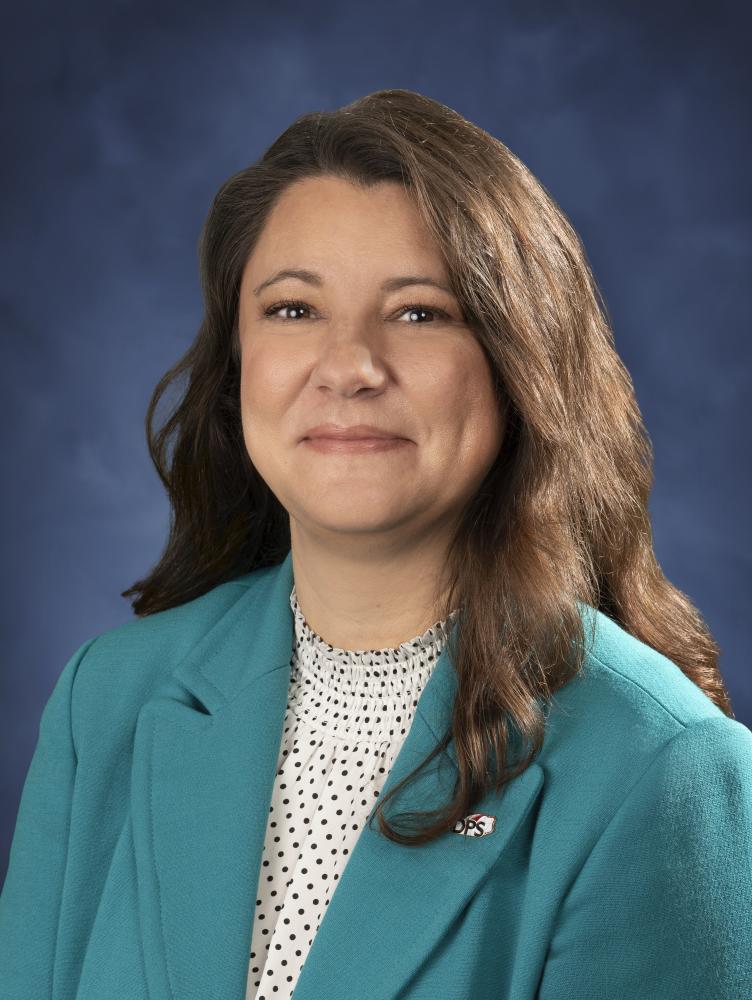 Melissa Earp (white female with brown hair) in blue suit jacket in front of blue background.