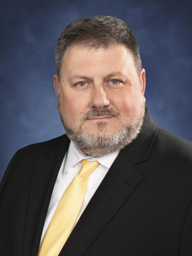 Eric Smith in black suit posed in front of blue background