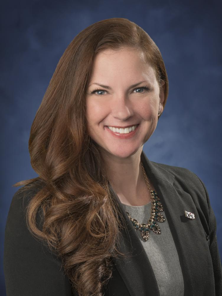 Susanna Davis (white female with long red hair) in grey suit in front of blue background