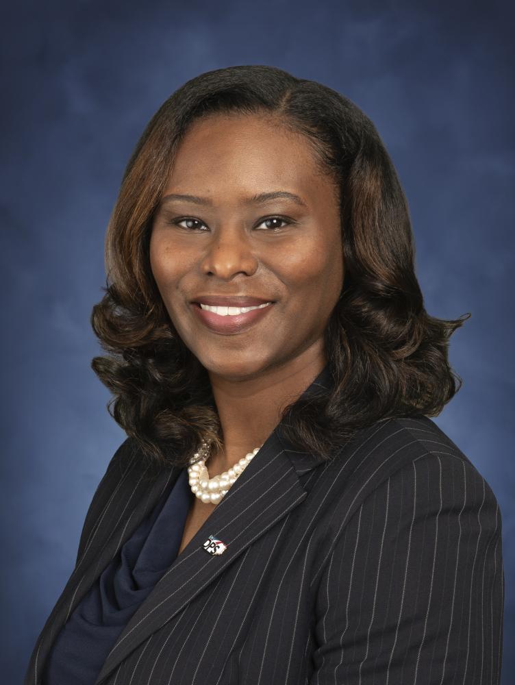 Black female wearing a black blouse, black pinstriped suit jacket and string of pearls.