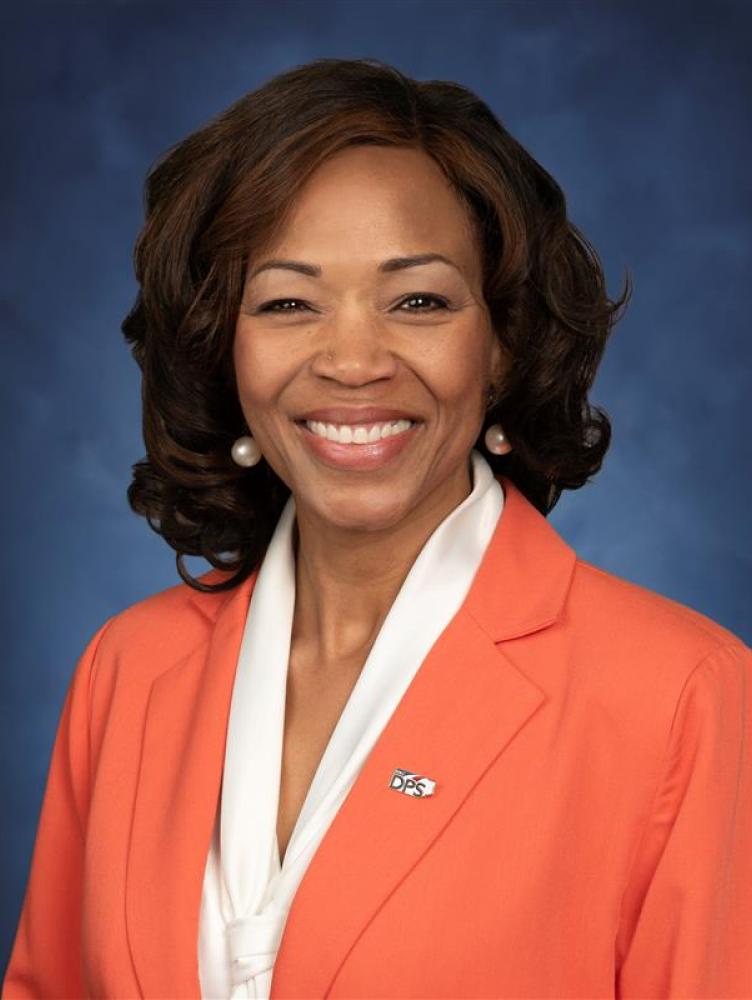 Black woman in orange suite jacket and white blouse.