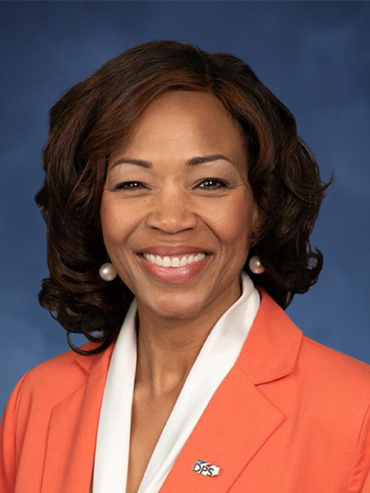Black woman with orange suite jacket and white blouse.