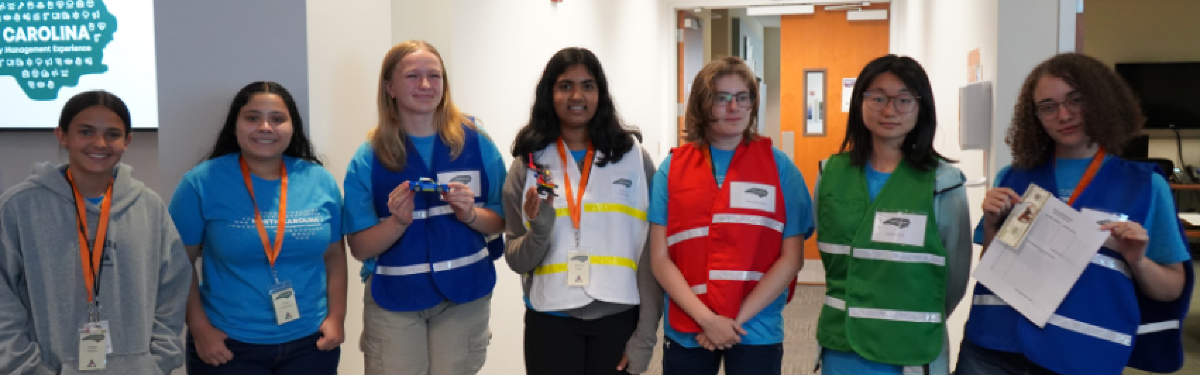 A group of young women standing together wearing blue, white, green, and red vests. 