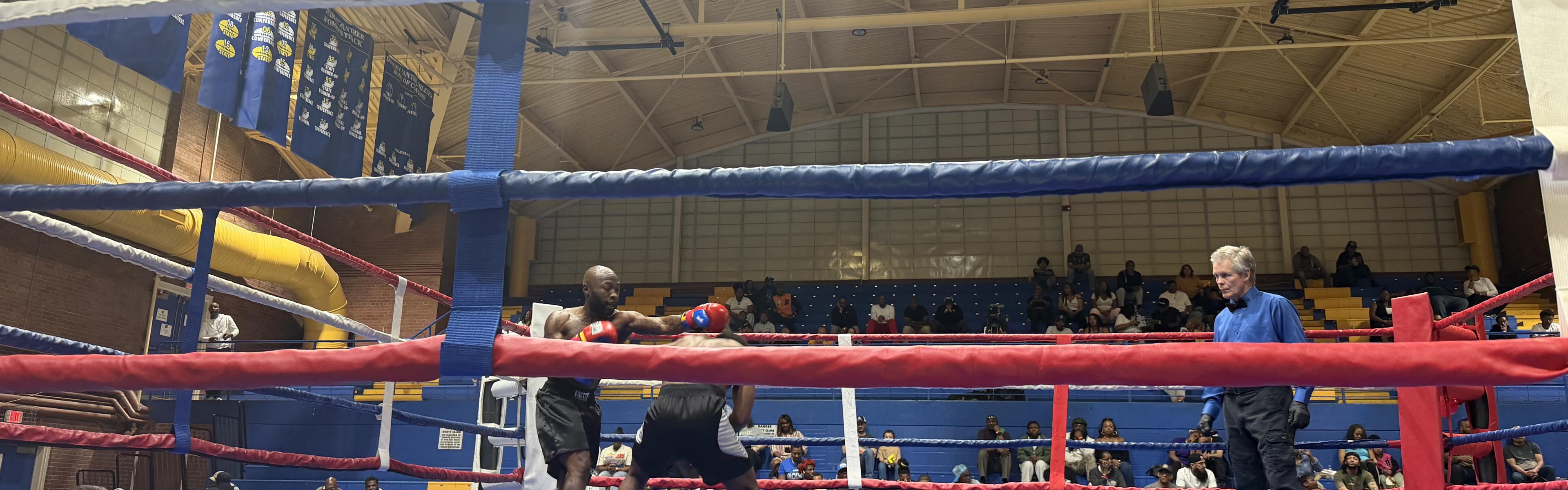A boxing match in progress at an indoor venue, with two boxers in the ring as the officiating referee watches