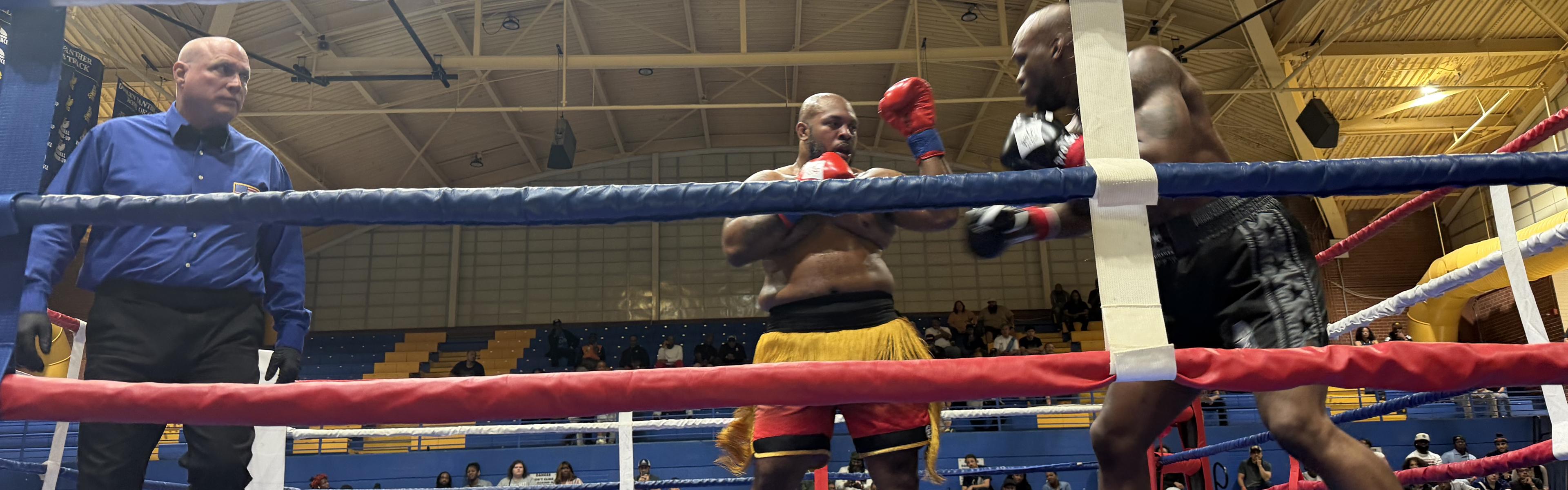 A boxing match in progress at an indoor venue, with two boxers in the ring and a referee officiating.