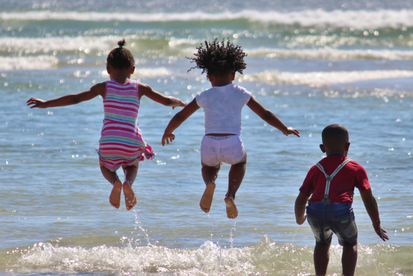 Three children jumping into waves on the beach