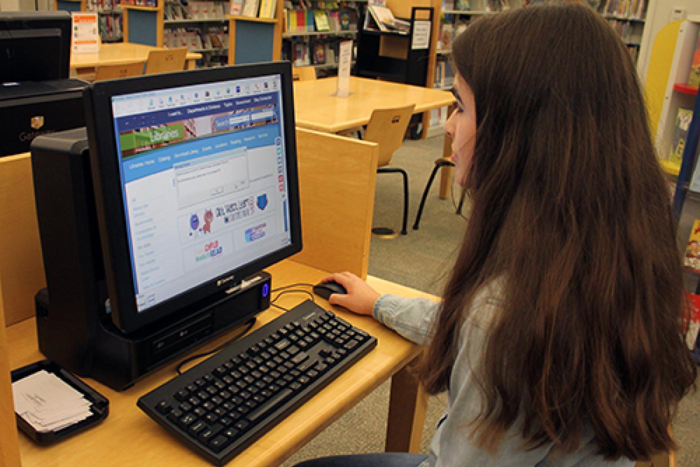 Young girl sitting in a library at a desktop computer.