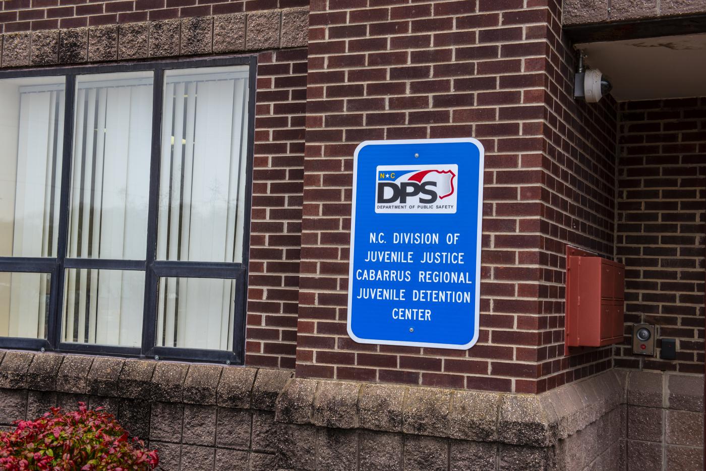 Blue sign with NCDPS Logo and the Juvenile Justice Cabarrus Detention Center name attached to a red brick building wall