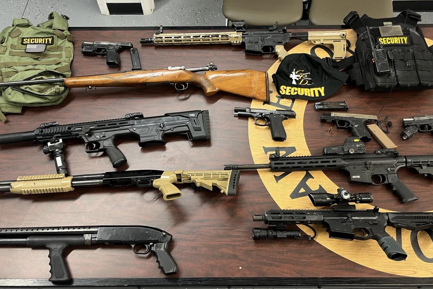 Rifles, shot guns, handguns with magazines and two tactical vests on wooden table