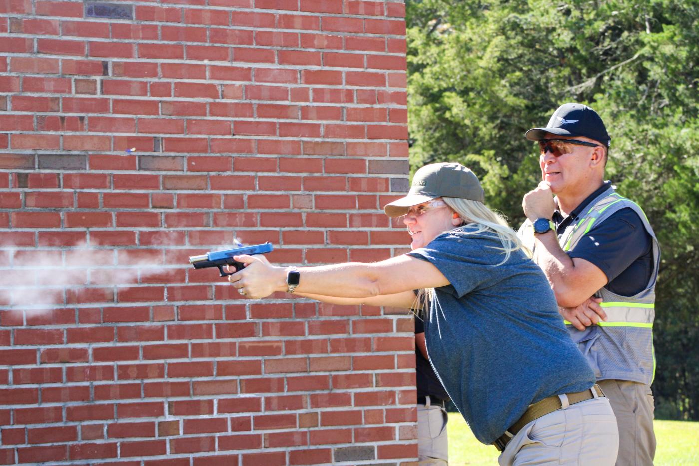 Female firing a gun down range. An instructor watches in the background.