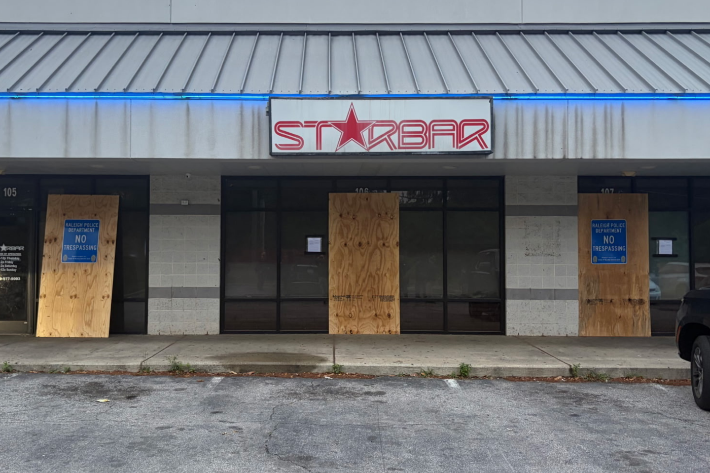 Grey strip mall with grey roof and plywood in front of doors
