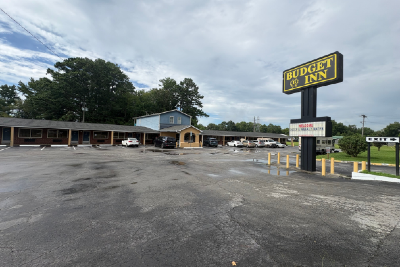 red brick motel with two story blue building in the middle with a black road sign