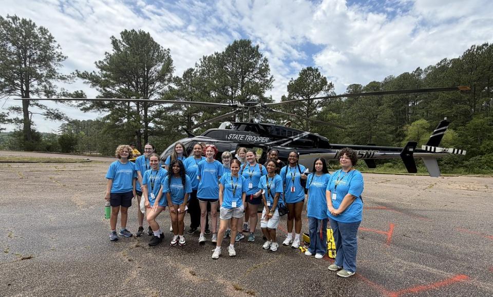 Group of young women wearing matching blue shirts standing in front of a helicopter.