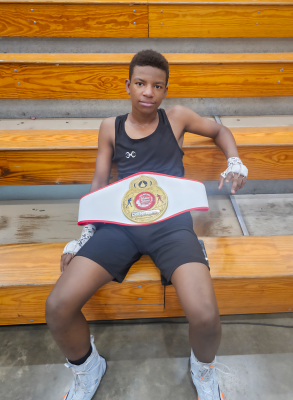 Young athlete in boxing gear sits on bleachers holding a championship belt