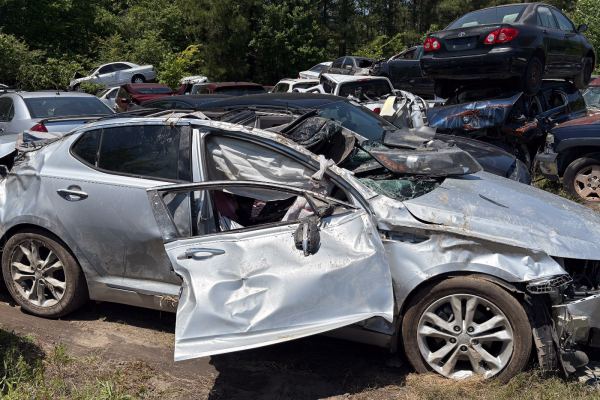 side view of a wrecked silver car with extensive damage to the roof and side