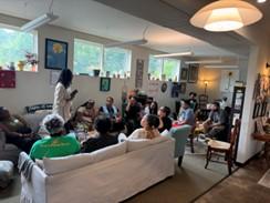 People sitting on couch and on chairs listening to a speaker standing the middle