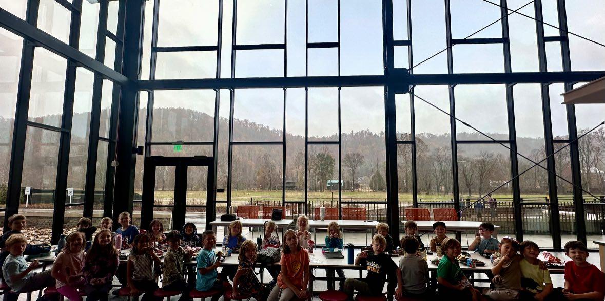 Young students sitting in a lunch room with floor-to-ceiling windows