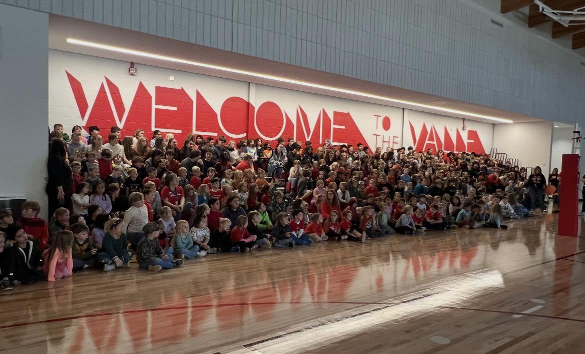 Many young children gather together in a school gymnasium