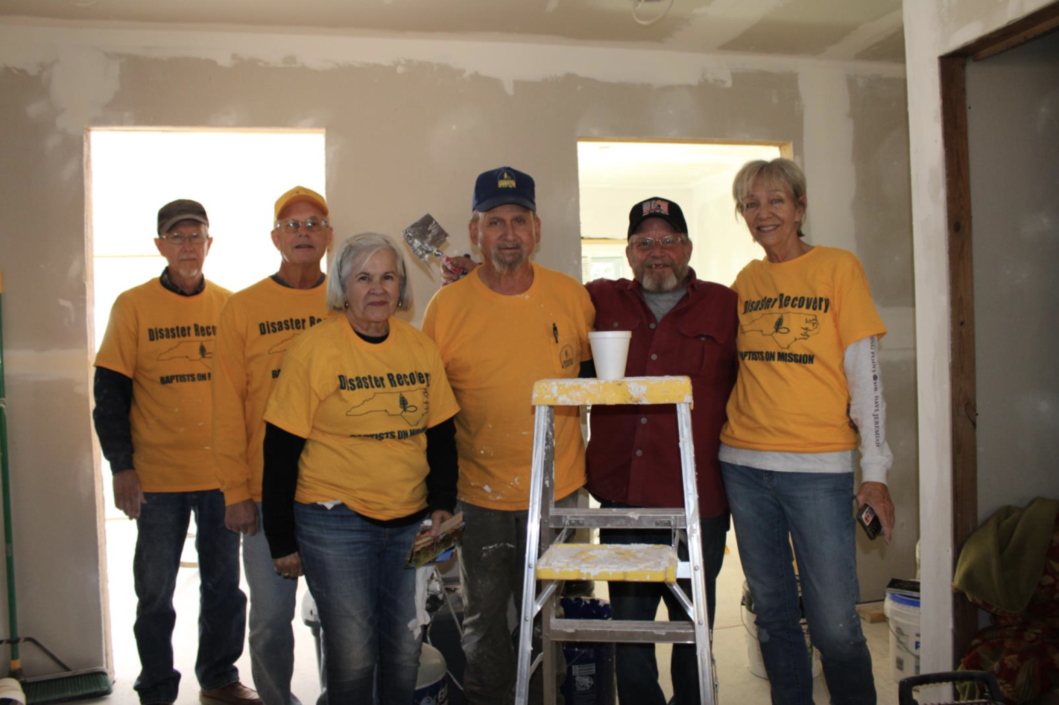 Five volunteers wearing bright yellow shirts pose behind a ladder