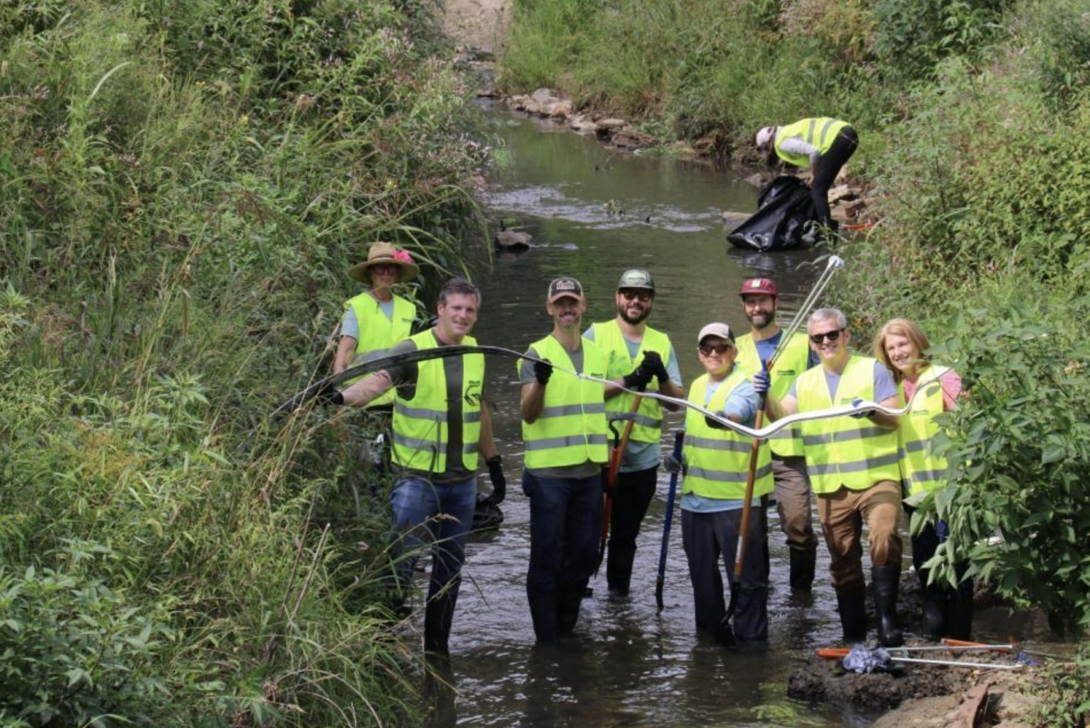 Eight people wearing reflective vests pull debris from a stream