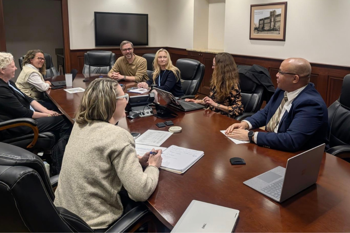 Six people sitting in a small conference room
