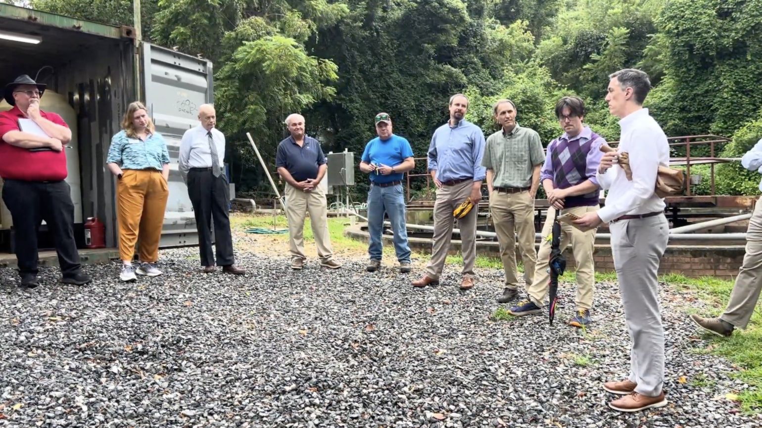 Ten people standing in a large circle on a gravel lot