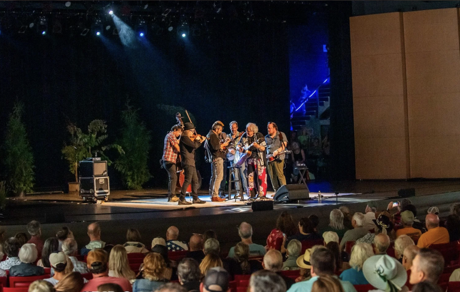 Seven-piece band performs on a stage in front of a large seated crowd