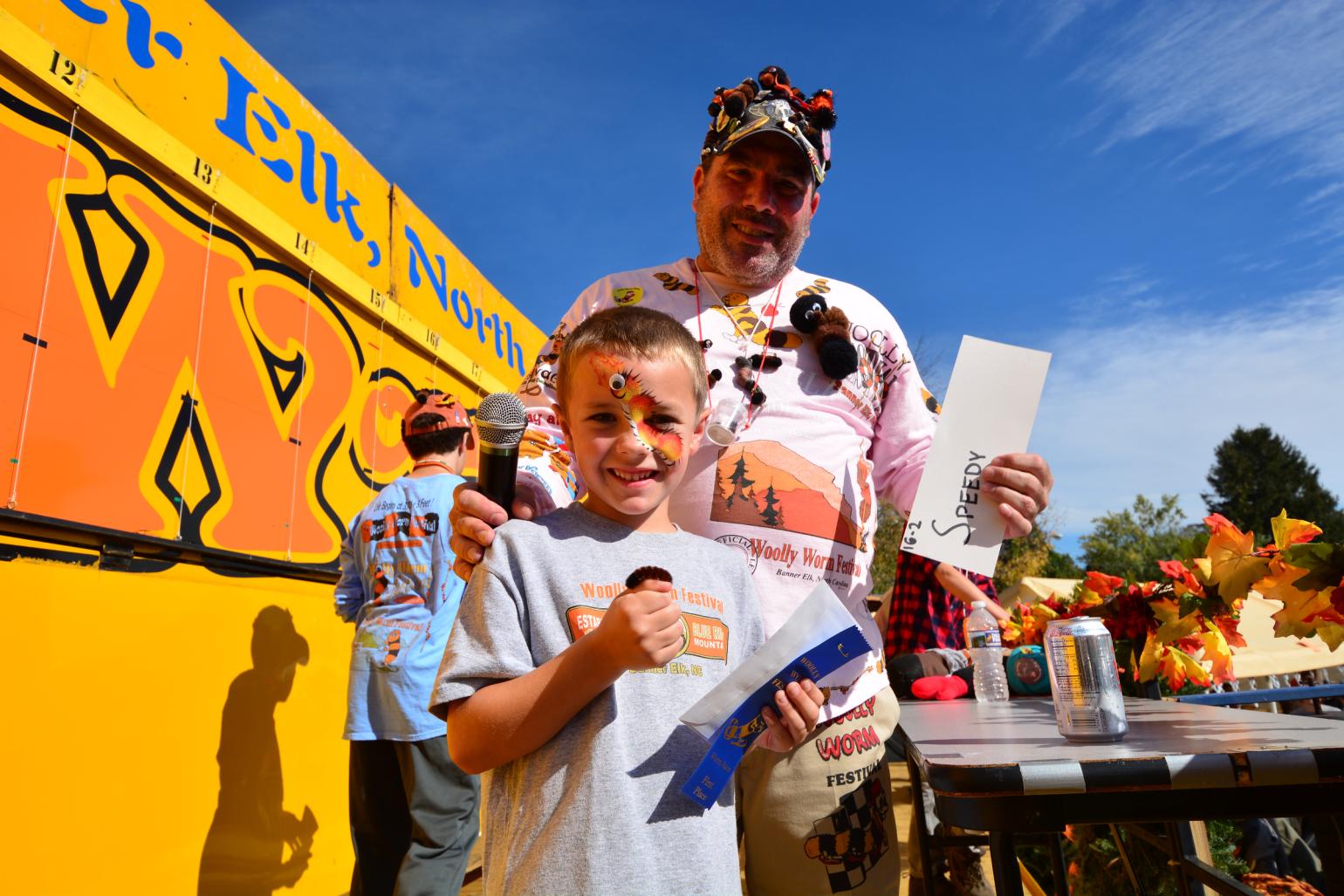 A man and child standing outdoors at a festival holding a small creature