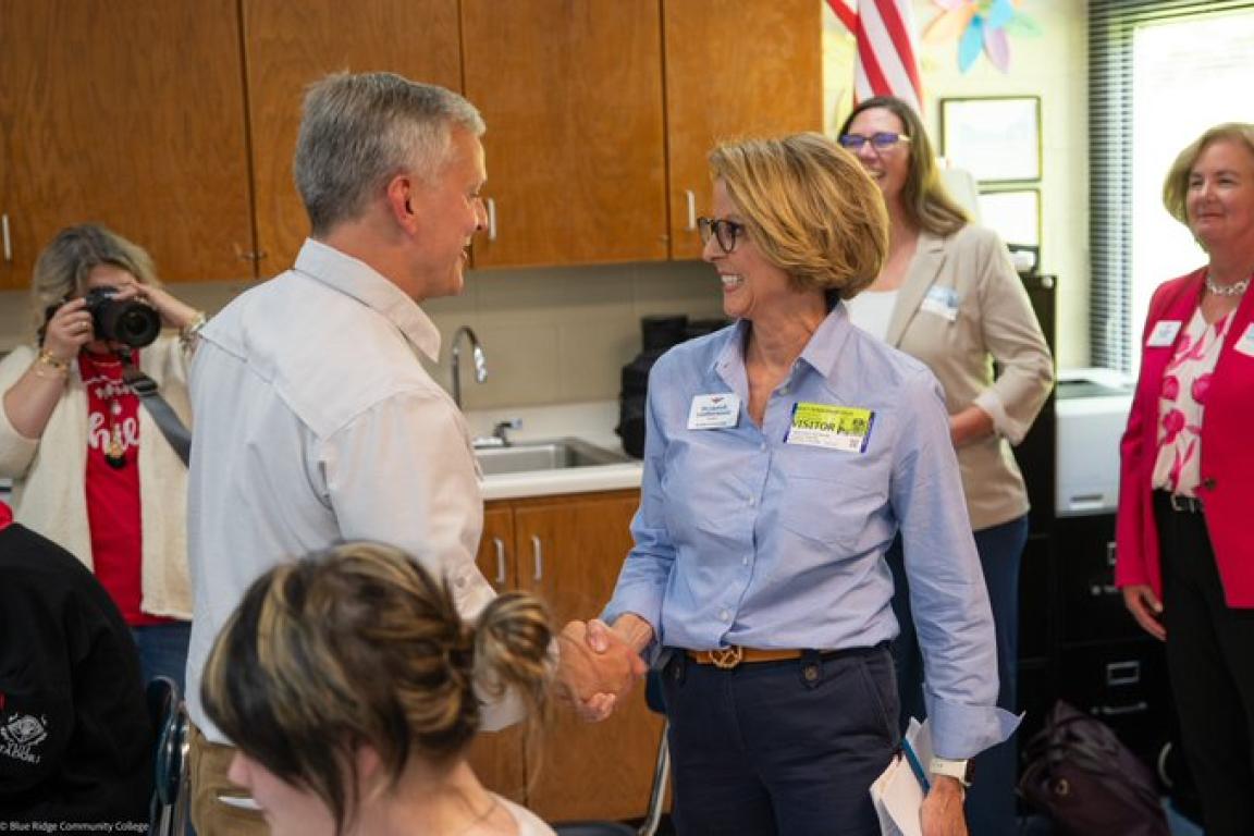 Two leaders shake hands in a room full of people