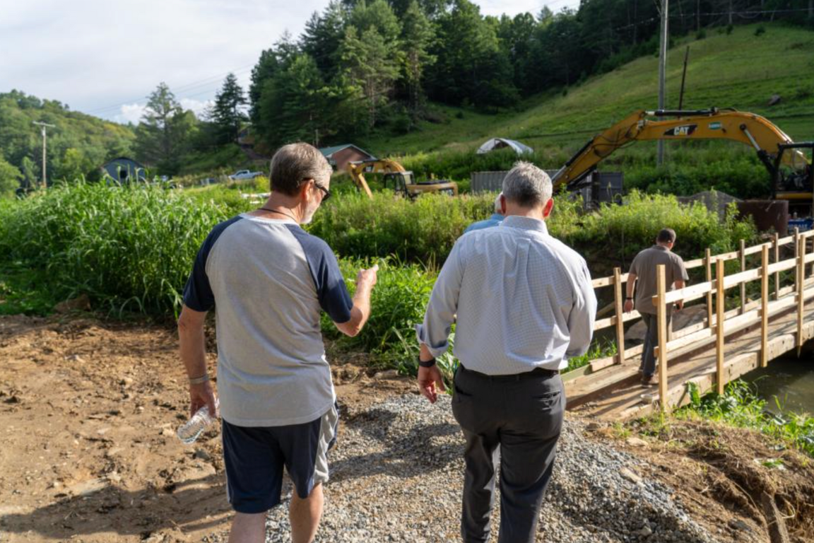 Two people assess a newly built bridge across a stream