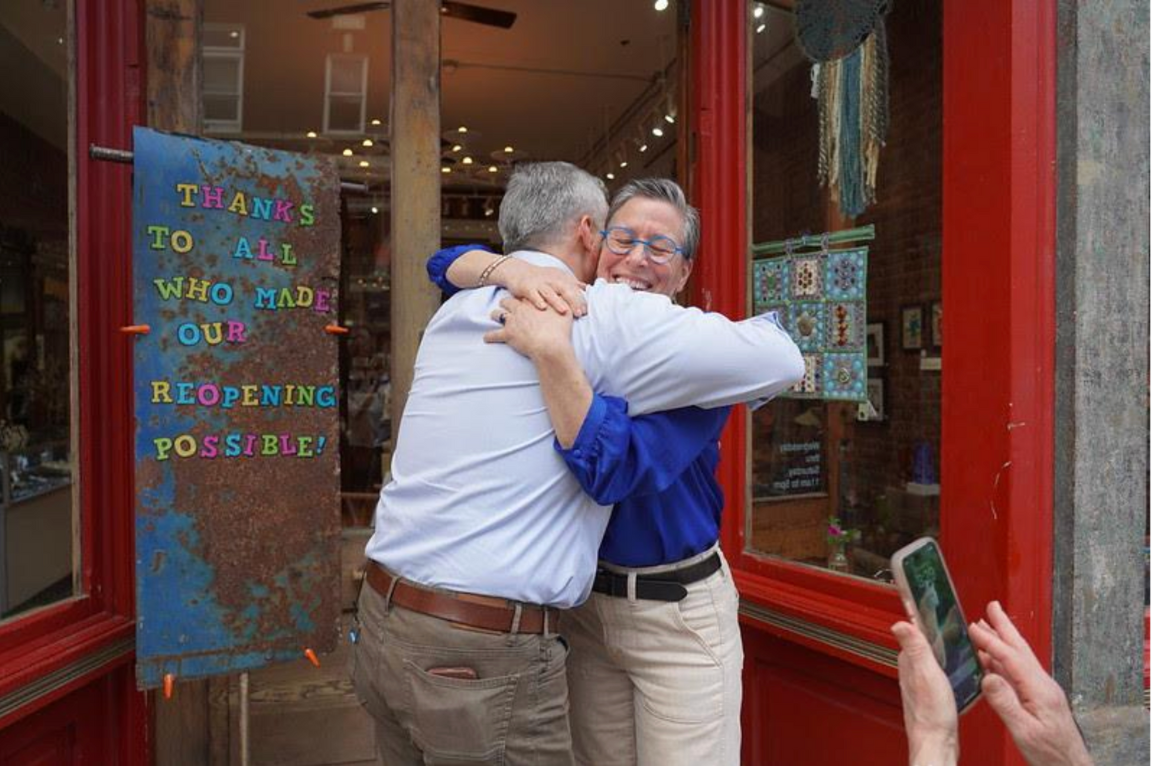 Two people hug in the doorway of a small business