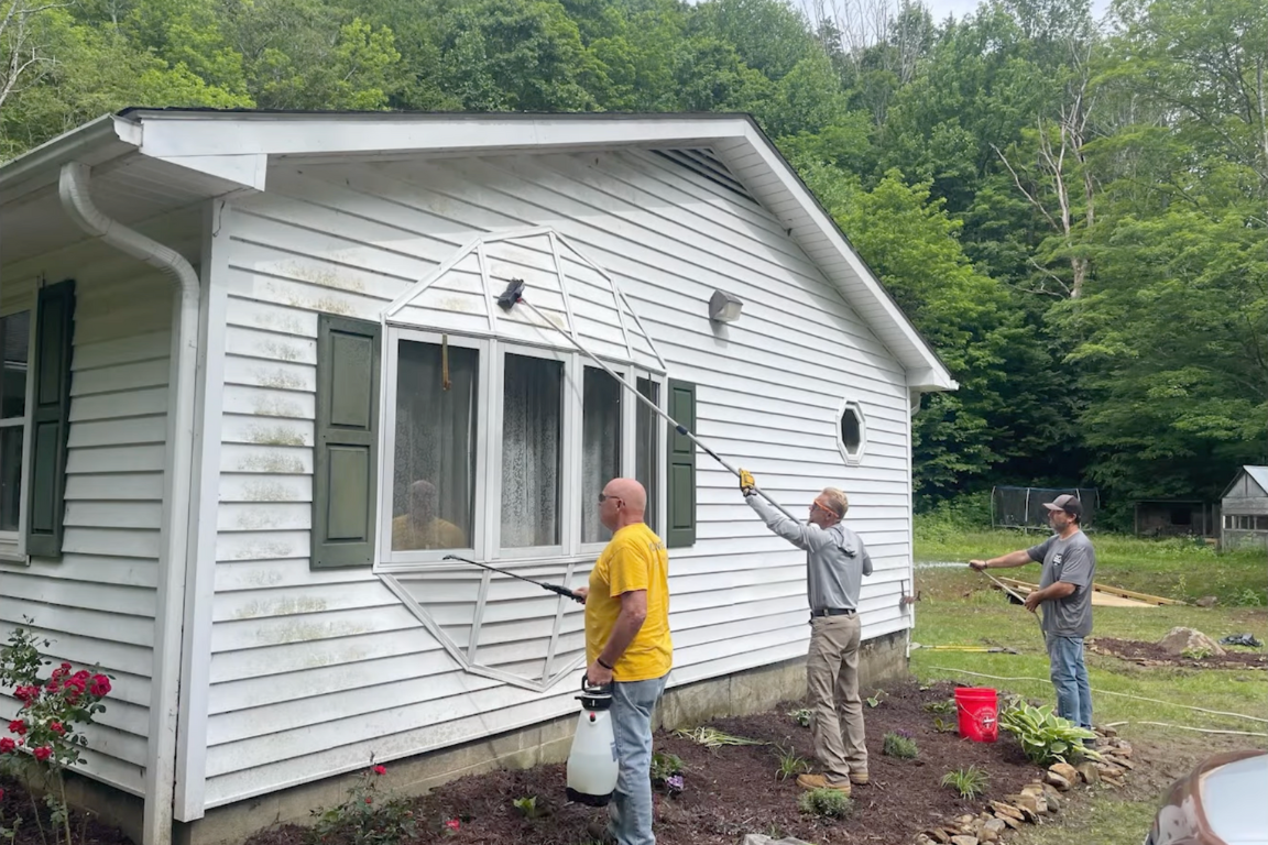 Three people power washing a one story home