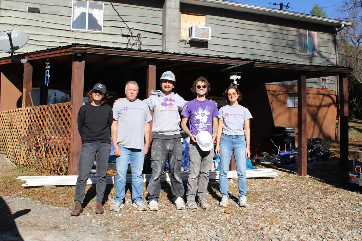 Five people pose outside of a home dressed for construction work