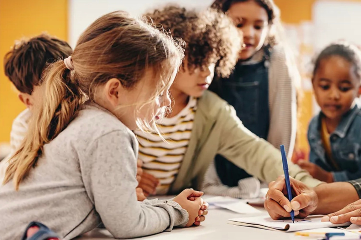Young children sit around a table in a classsroom setting