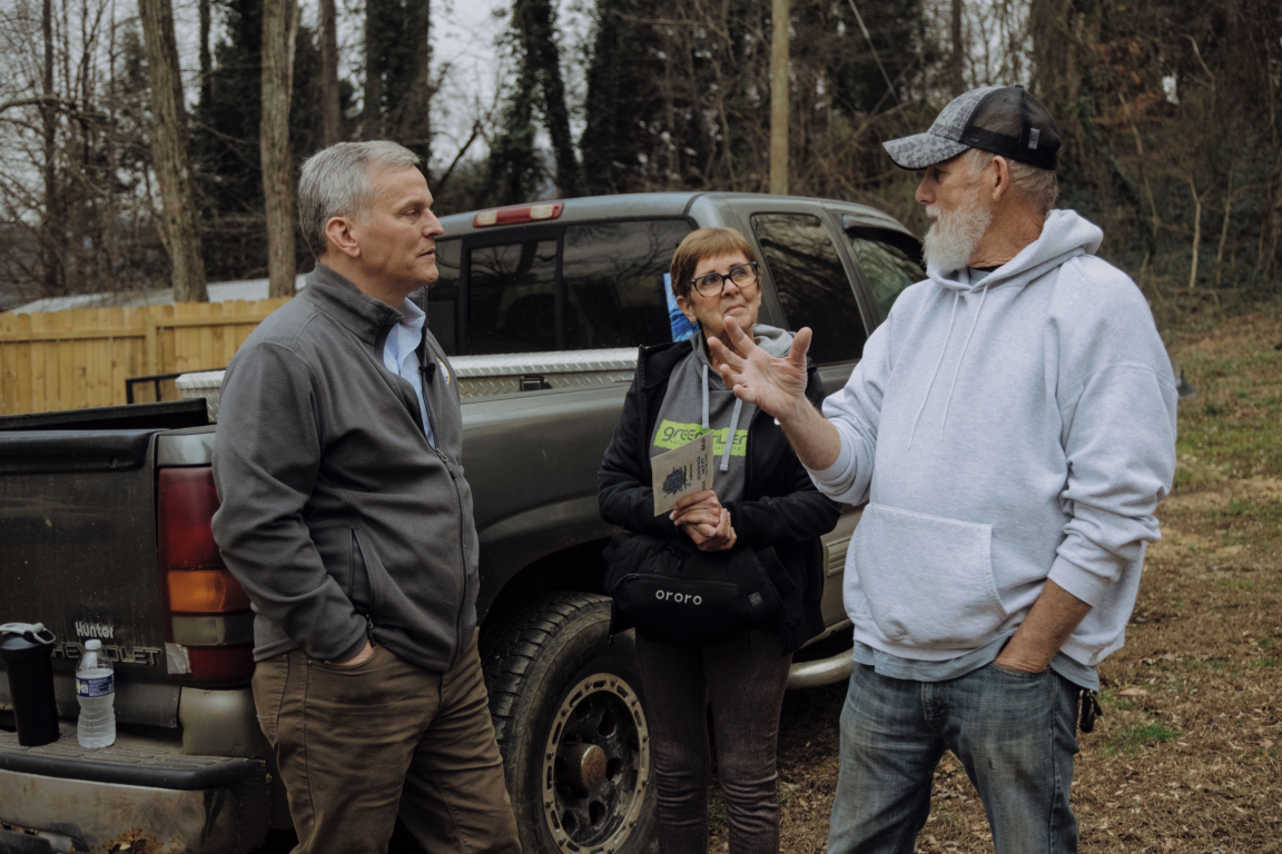 Three people in conversation near a work truck in an outdoor setting