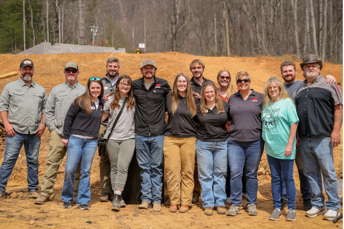 A large group of volunteers pose for a photo in front of a home construction project