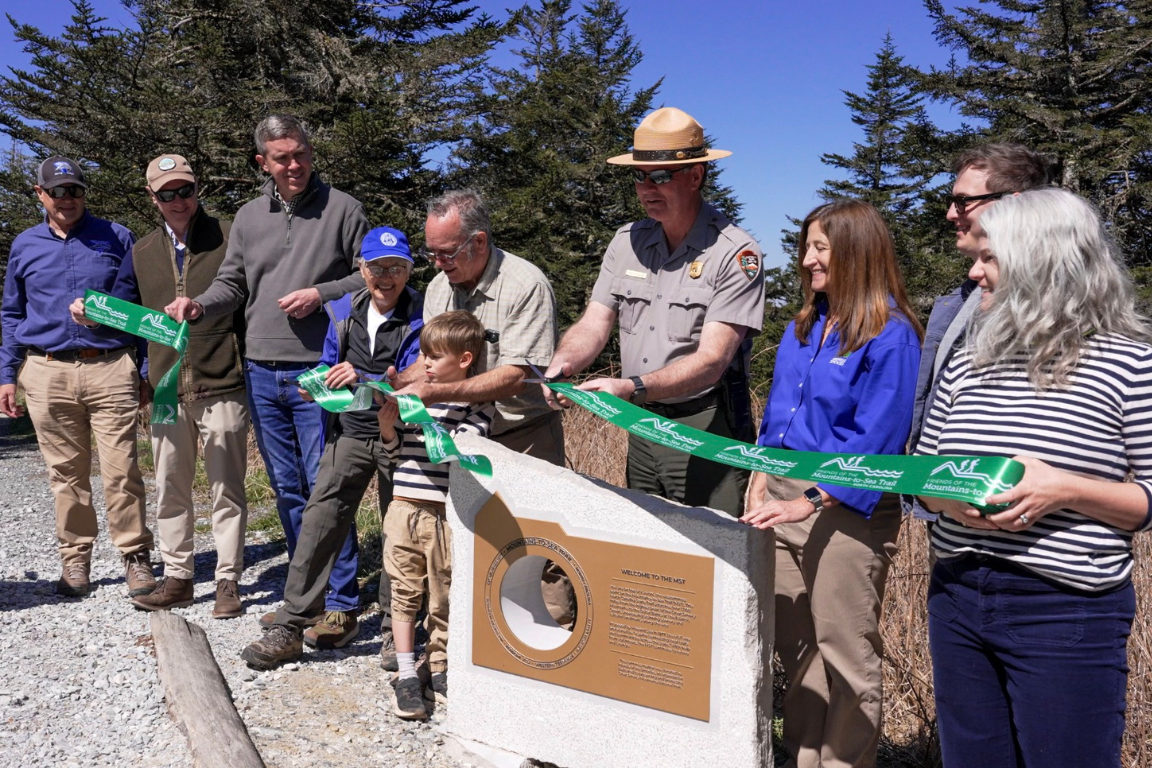 Ten people standing outside for a ribbon-cutting on a clear day