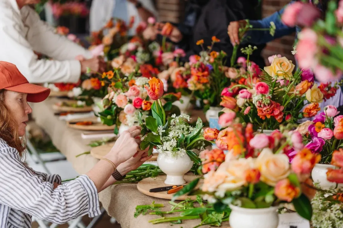 People sit around a table arranging flowers into vases