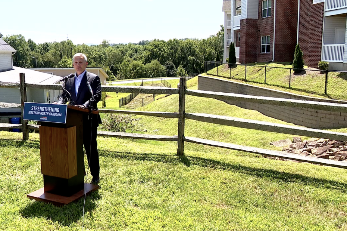 Man stands at a podium in a field in front of an apartment building