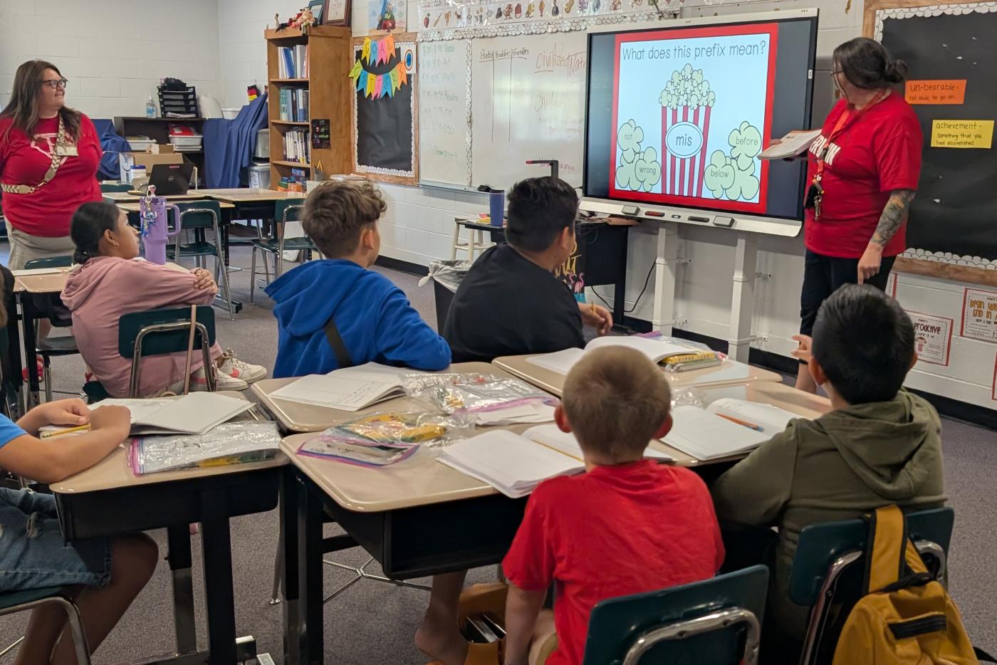 young students sitting at a table while listening to a teacher