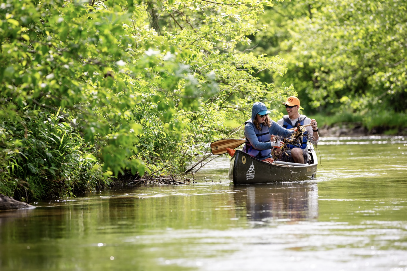 Two people float in a canoe along the French Broad River