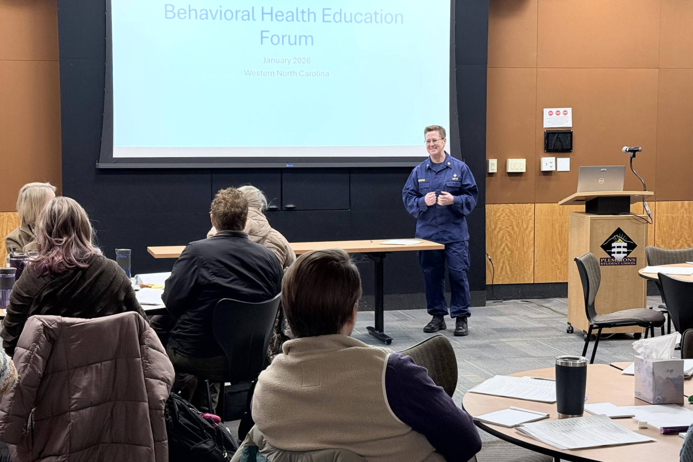 Woman dressed in blue addresses seated event attendees