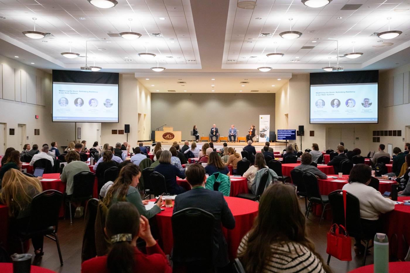 Large room of conference attendees listen to four-person panel seated on stage