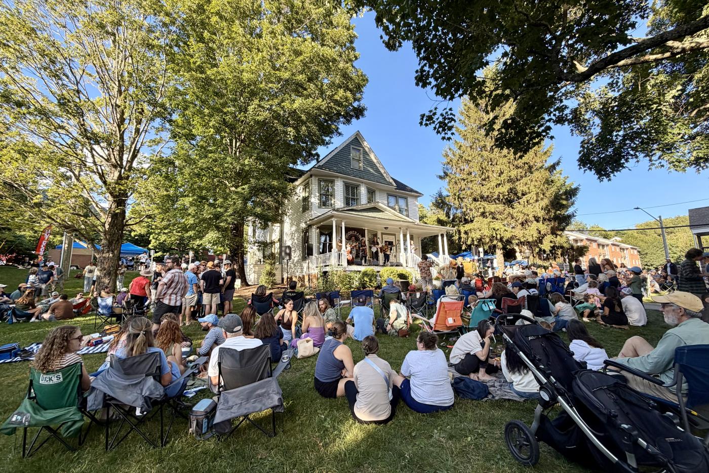 Crowd of people sitting on the lawn of a house, listening to live music from the porch