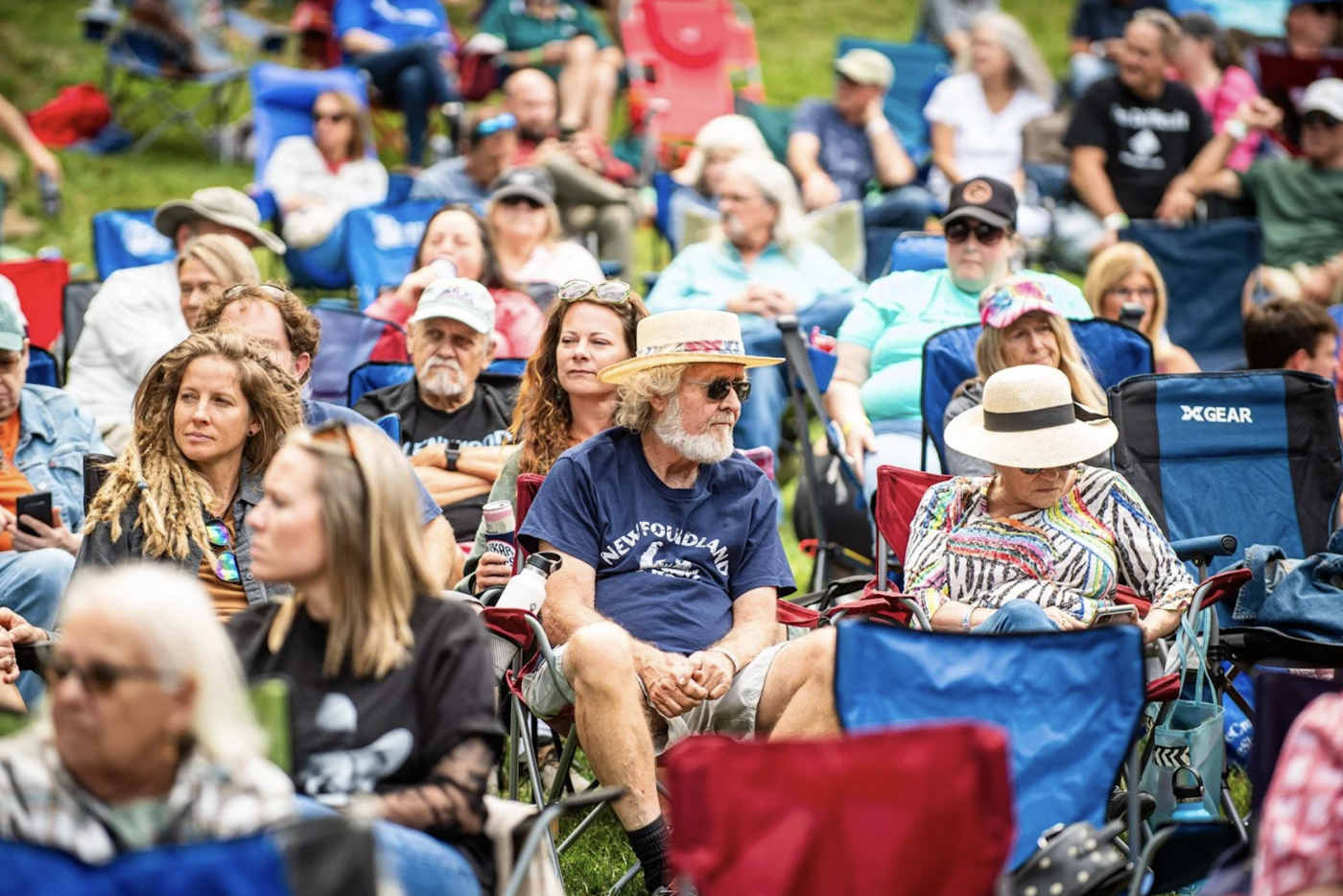 Crowd seated in chairs in a grassy area at an outdoor music festival