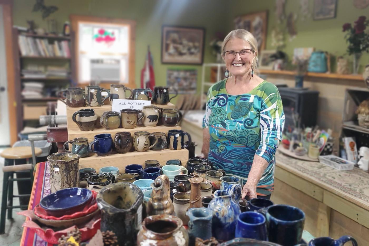 Casually dressed woman poses among completed pottery projects