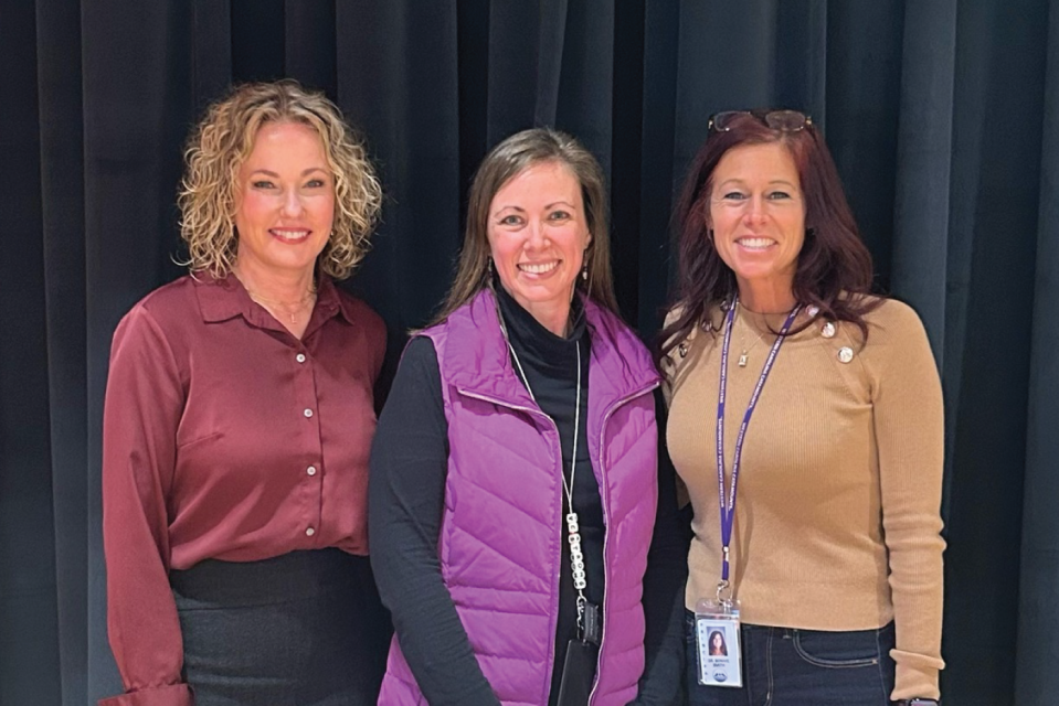 Three women pose in front of a stage curtain searing ID badges